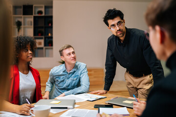 Portrait of successful business team leader standing surrounded by multiracial colleagues, confident looking at camera. Multiethnic startup business team posing at table in modern meeting office room.