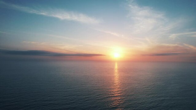 Fixed drone clip of calm blue sky with orange pink sunset over open ocean with views to the horizon