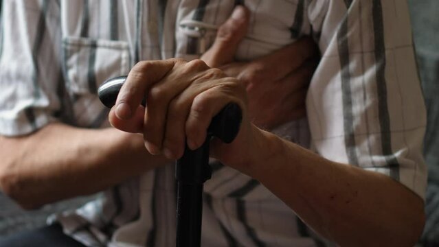 an elderly man sitting with a walking stick holds his hand to his sick heart while at home.selective focus. an elderly man is suffering from chest pain in the heart. be healthy