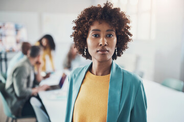 Young businesswoman standing in a boardroom with colleagues talking in the background