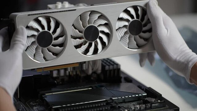 Close-up hands of unrecognizable male gamer in rubber gloves installing new graphics card of latest model on motherboard. Stages of upgrading or assembling desktop computer. Shooting in slow motion.
