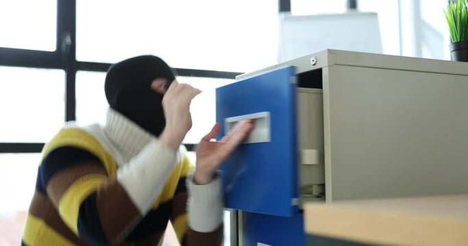 Young man in balaclava steals information from an office. Theft of valuable documents in the company