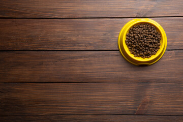Pet care concept. Bowl of dry food on wooden background. Top view.