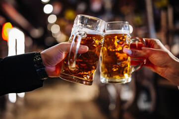 man and woman hands clinking with glasses of light beer at the pub or bar