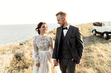a young wedding couple after the ceremony walks on a hilltop overlooking the sea. bearded groom with beautiful bride. wedding walk couples holding hands