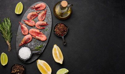 Boiled shrimp on a board, lemon slices, spices on a black background, top view