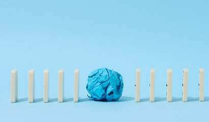 Row of dominoes and crumpled paper ball on blue background