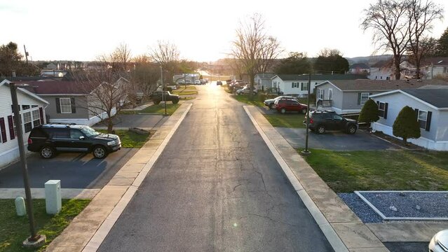 Cars parked in quiet low income neighborhood in America. Mobile home trailer park with sunlight reflecting on street in winter golden hour.