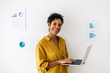 Female data analyst standing in an office and using a laptop