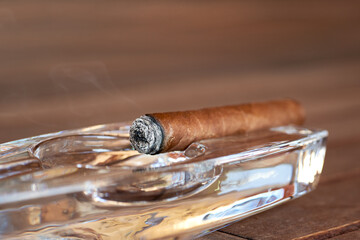 Burning Cuban cigar in a glass ashtray