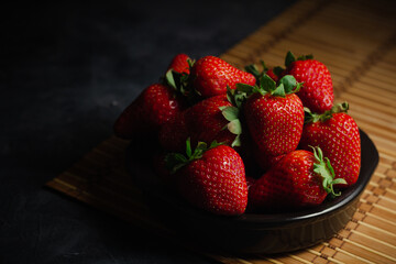Delicious fresh strawberries with green leaves placed in black bowl on wooden table
