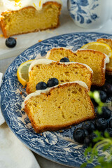 Slices of homemade lemon pound cake decorated with cream cheese frosting, fresh lemon slices and blueberries on vintage blue plate .