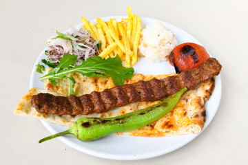 Grilled Turkish Adana, Urfa  Kebab with grilled vegetables, onion and rice on plate. Adana durum.
