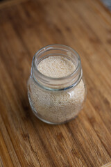 Cane sugar in a small glass jar set on a wooden kitchen board. Close up shot, top-side view, no people