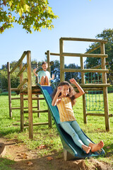 Carefree brother and sister playing on slide at playground structure