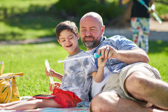 Father and cute son with Down Syndrome playing with bubble wand