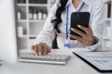 Fototapeta premium Portrait of Asian businesswoman talking mobile phone and working on laptop and papers on table in her office.