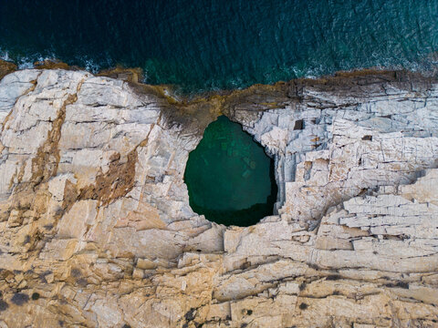 Aerial view of Giola on the Greek island of Thassos. The natural swimming pool's crystal-clear turquoise waters, surrounded by rocky cliffs and lush greenery, create a mesmerizing visual spectacle.