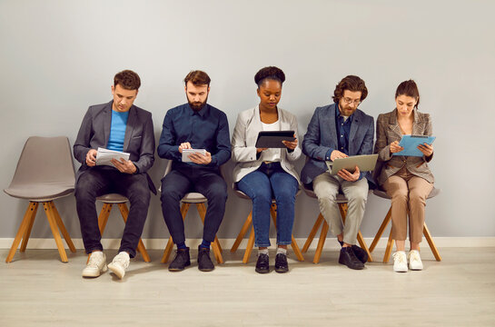 Carried away peoples men and women carefully study papers waiting in line for interview with employer want to get good offer from large company sits along wall in bright room. Career, business