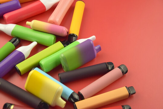 Set of multicolor disposable electronic cigarettes on a red background.