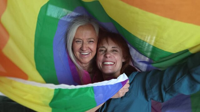 Happy senior women having fun with gay pride rainbow flag, mature lesbian women.