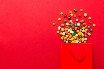 shopping paper gift bag in corner full of assorted traditional candies falling out on colored background with copy space. Happy Holidays sale concept