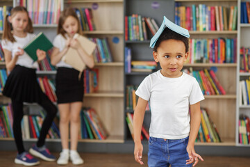 Back to school. Mixed-race schoolboy with book on head having fun.