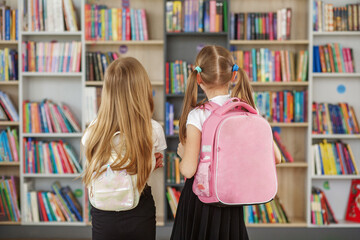 Two children choose books in school library. Books on shelves in bookstore. Children with backpacks.