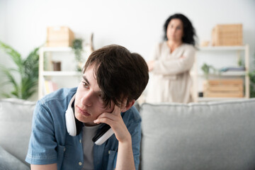 Frustrated boy sitting on sofa and mother looking at him