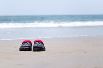 the shoes kept near the beach with waves of ocean are in the background