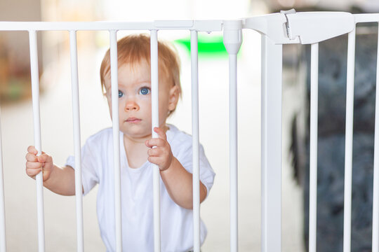 Sad little girl standing at locked baby safety gate and fence