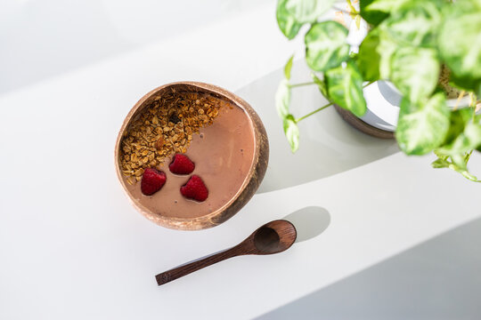 fresh berry smoothie bowl for breakfast in coconut shell bowl with wooden spoon and plant