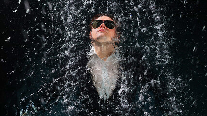 Fototapeta premium A man in a suit and sunglasses dives into the water in the rain.