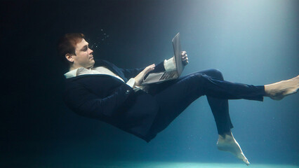 Businessman in a suit is working on a laptop and drowning under water.