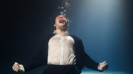 A businessman, a man in a suit, screams underwater.