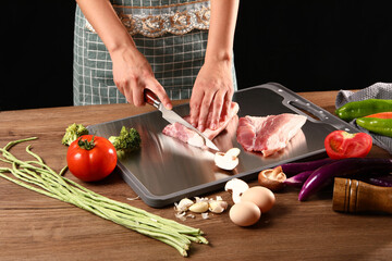 Chef slicing meat on stainless steel cutting board in kitchen with various vegetables next to it,...