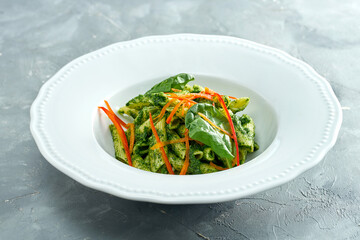 Vegetarian pasta with spinach and pepper in a white plate on a gray background