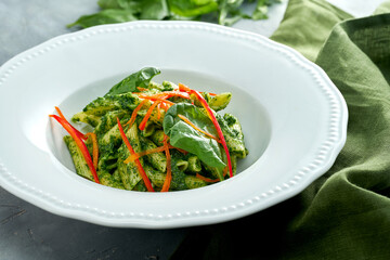 Vegetarian pasta with spinach and pepper in a white plate on a gray background