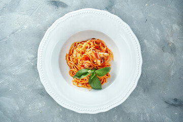 Italian spaghetti pasta with tomatoes and shrimps in a white plate on a gray background