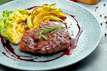 Grilled beef steak with a side dish of cabbage and sauce in a plate on a gray background