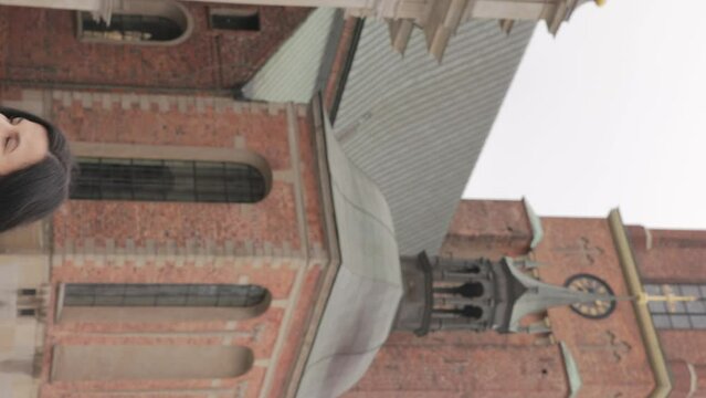 Vertical Shot Of A Woman Walking Outside The Riddarholmen Church With Brick Tower And Cast Iron Spire In Background. tilt-up