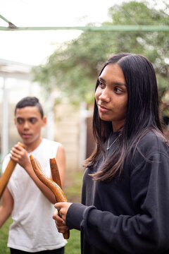 Aboriginal teenage girl with musical sticks in her backyard  with her brother