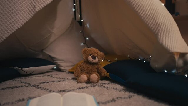 Teddy bear toy, pillows and book lying in a blanket fort, happy childhood