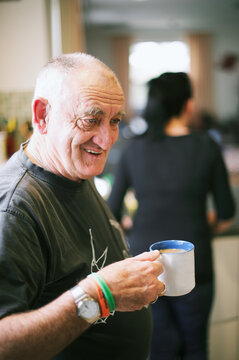 A Man in his 60s Standing Holding a Mug of White Tea, smiling.