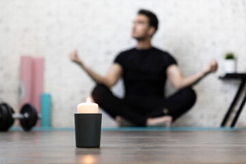 Close-up of candle with practicing yoga in lotus pose man on background. Yoga poses and stretching concept	