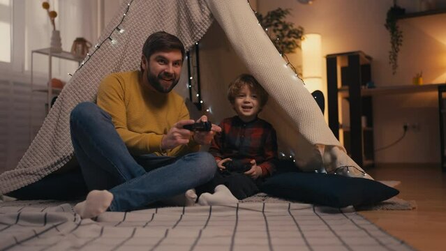 Dad and his little son playing video games together at home, family togetherness
