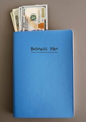 Blue notebook, money cash dollars with written text BUSINESS PLAN document that defines in detail a company's objectives and how it plans to achieve its goals