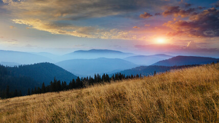 Amazing panoramic landscape in the mountains at sunrise. View of colorful sky and foggy hills covered by forest. Concept of the awakening wildlife.