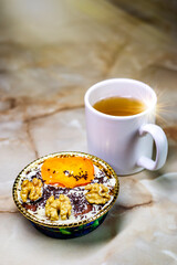 A cup of black tea on the table with a plate of cookies, chocolate and nuts