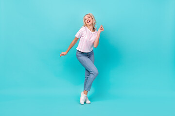 Fototapeta na wymiar Full length photo of satisfied adorable lovely girl wear striped t-shirt denim pants dancing isolated on vivid turquoise color background